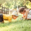 Caucasian girl and boy looking at plants grass in park through magnifying glass.