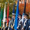 Military color guard members stand in formation holding U.S. and service flags during a veterans ceremony outdoors.