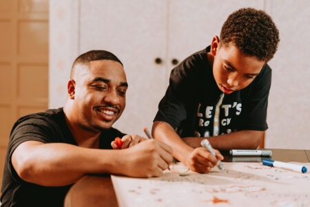 Adult and child drawing together at a table covered with paper and markers during a creative activity at home.
